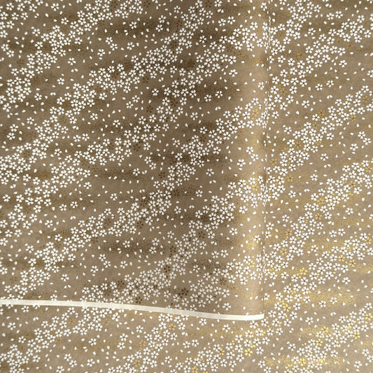 a sheet of Japanese silkscreen printed chiyogami paper with waves of tiny white and gold flowers on a soft taupe background with a dusting of gold.