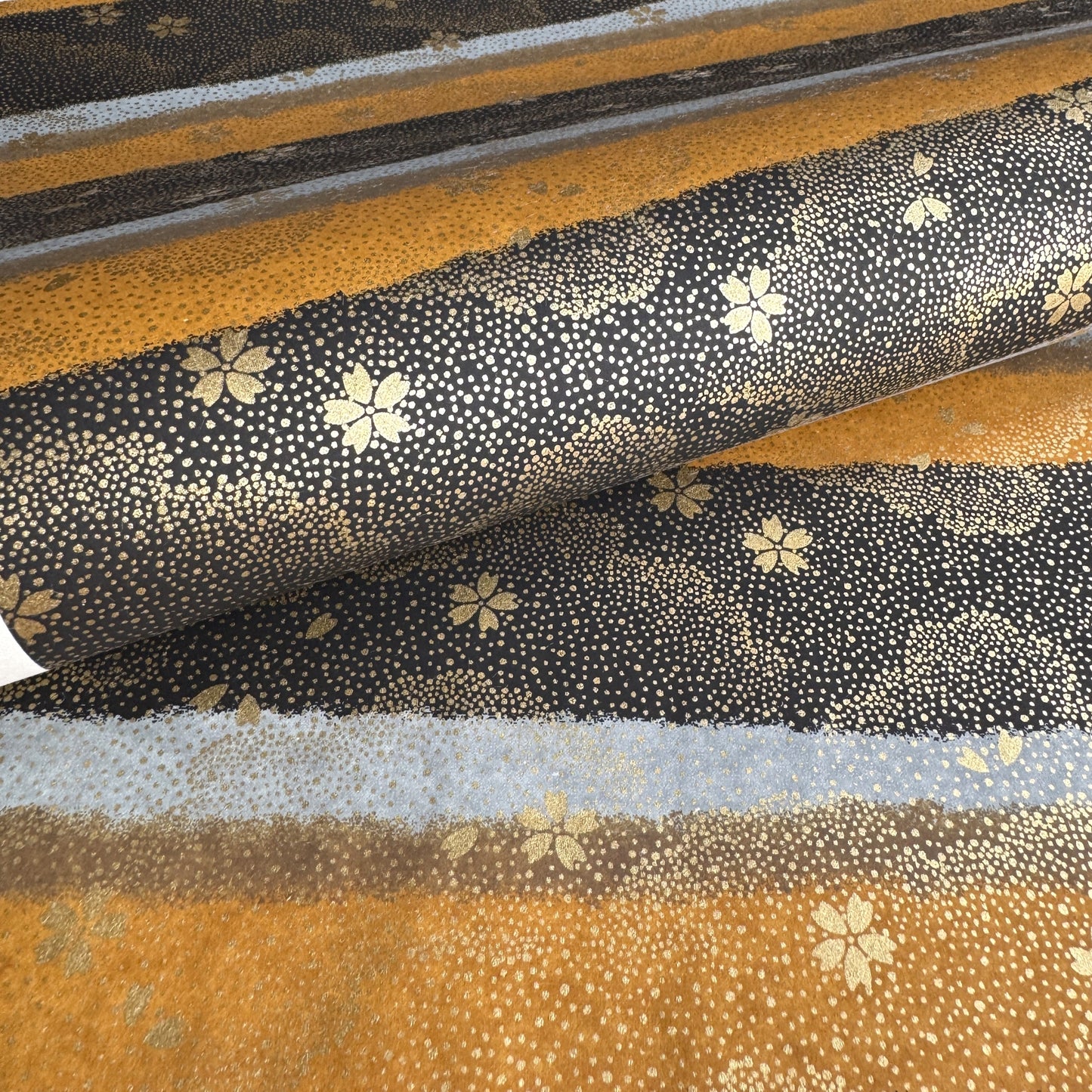 japanese chiyogami paper in stripes of black, brown, ochre and grey with gold clouds and flowers