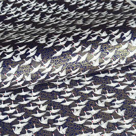 Japanese chiyogami paper with a silkscreened pattern of white cranes in flight on a midnight blue and gold background.