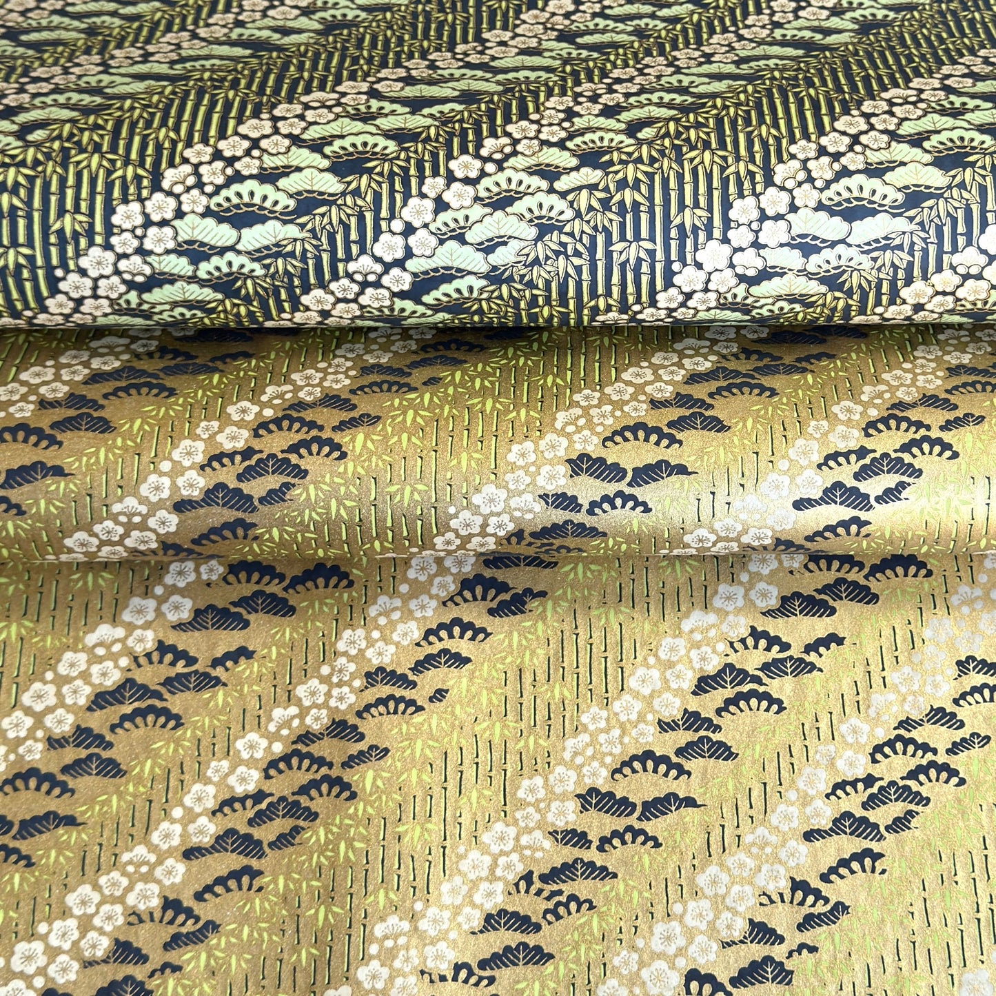 Japanese chiyogami paper with a design of trees, bamboo and plum blossom in indigo, green and white on a vintage gold backdrop.