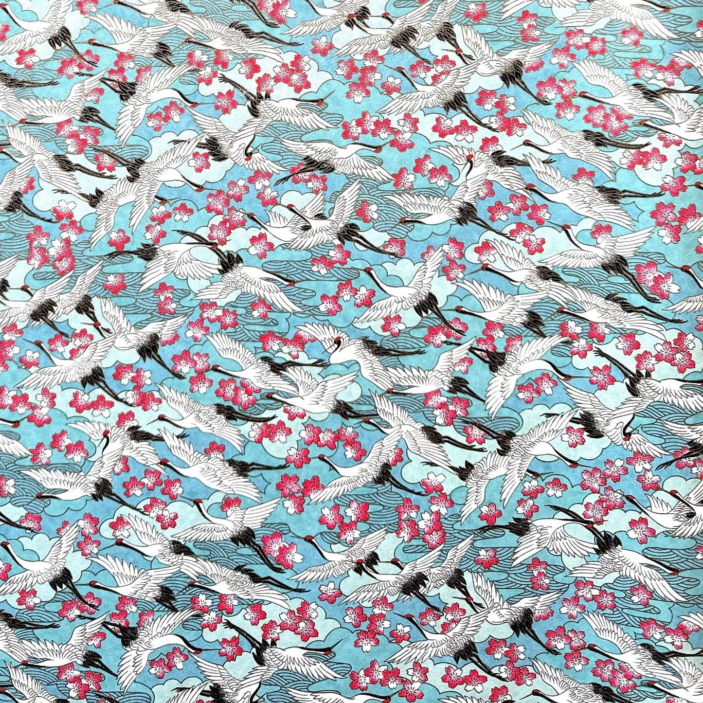 Japanese chiyogami paper with a pattern of white cranes, pink cherry blossom on a blue background.