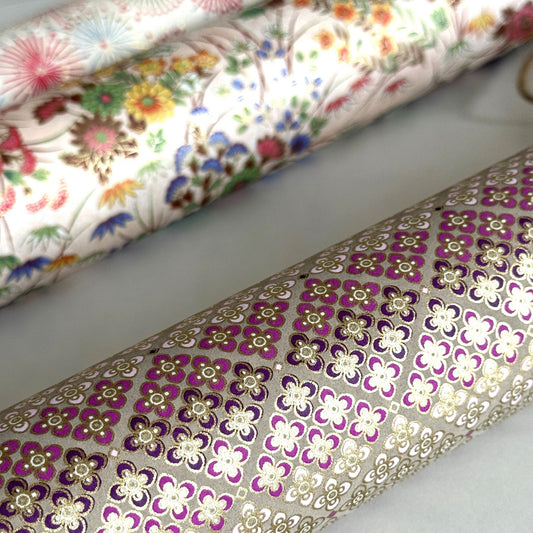 Japanese chiyogami silkscreen printed paper with rows of small flower motifs in purple, lilac and white on a taupe background with gold accents. Close up