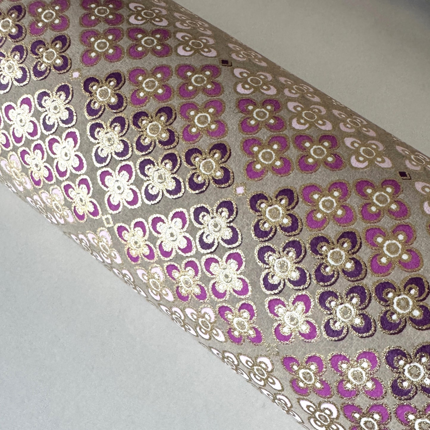 Japanese chiyogami silkscreen printed paper with rows of small flower motifs in purple, lilac and white on a taupe background with gold accents. Close-up