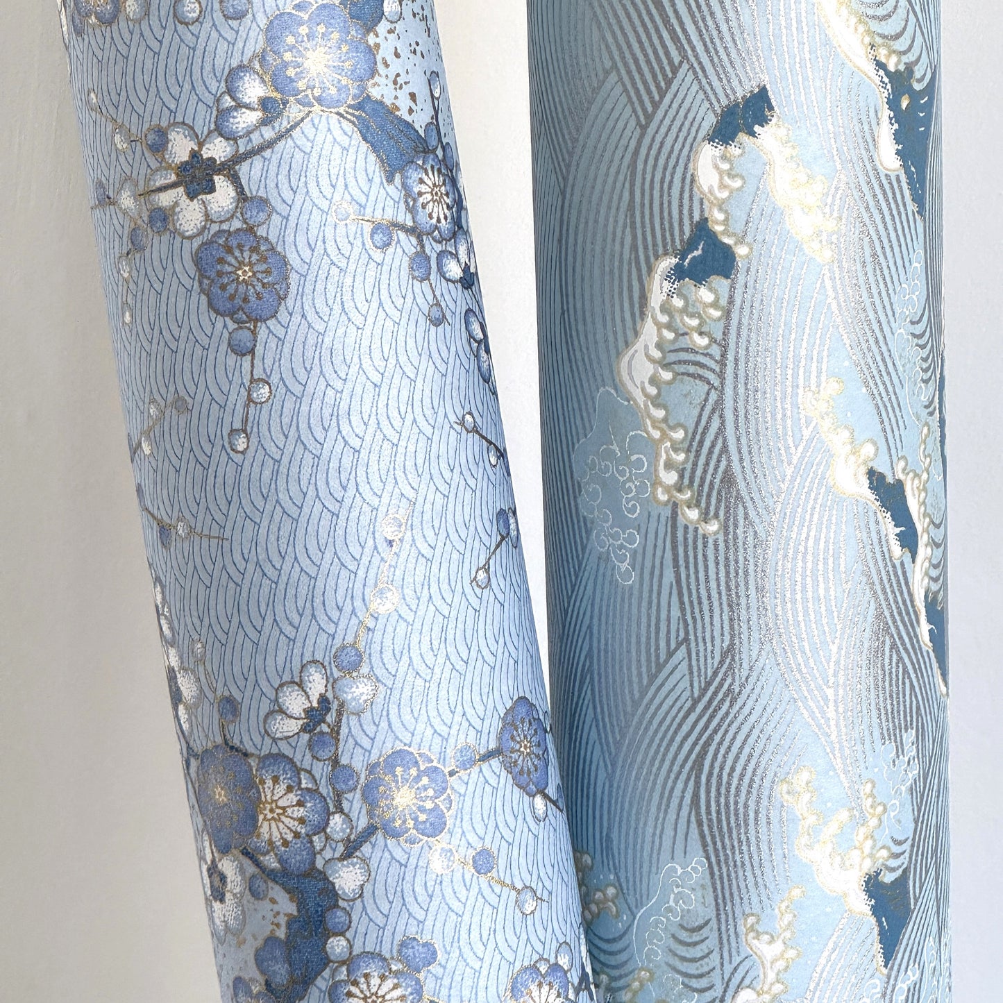 Japanese chiyogami paper with a wave pattern in pale blue, gold and silver. Rolled and pictured with another design from the collection