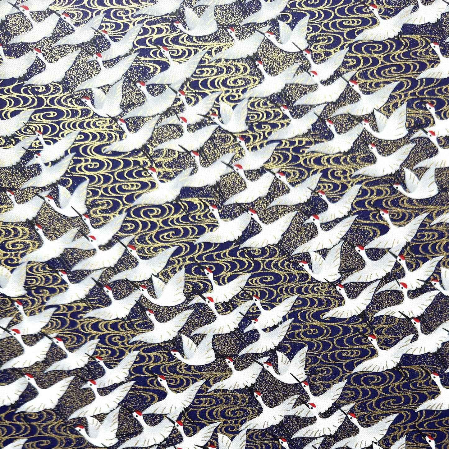 Japanese chiyogami paper with a silkscreened pattern of white cranes in flight on a midnight blue and gold background.