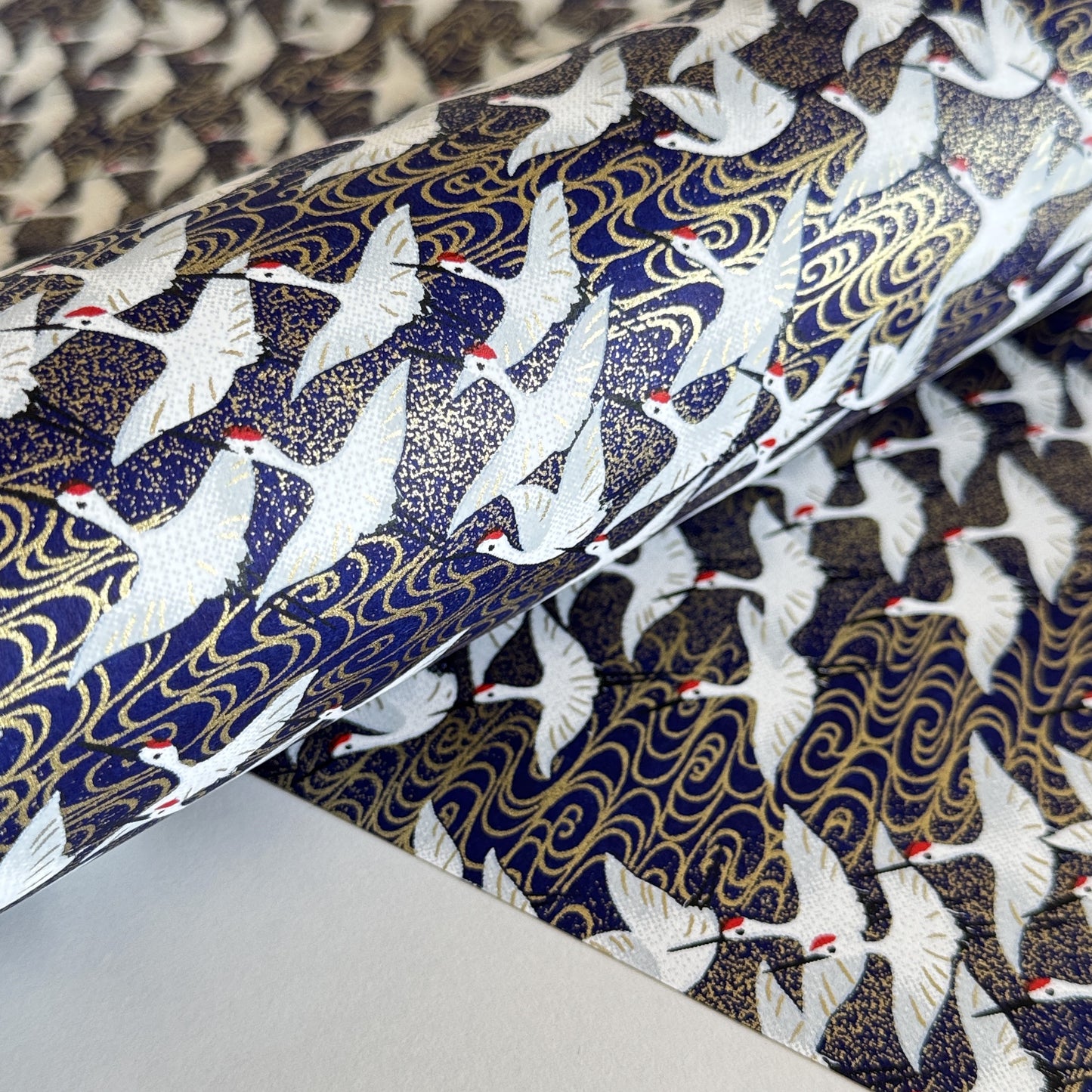 Japanese chiyogami paper with a silkscreened pattern of white cranes in flight on a midnight blue and gold background. Close-up