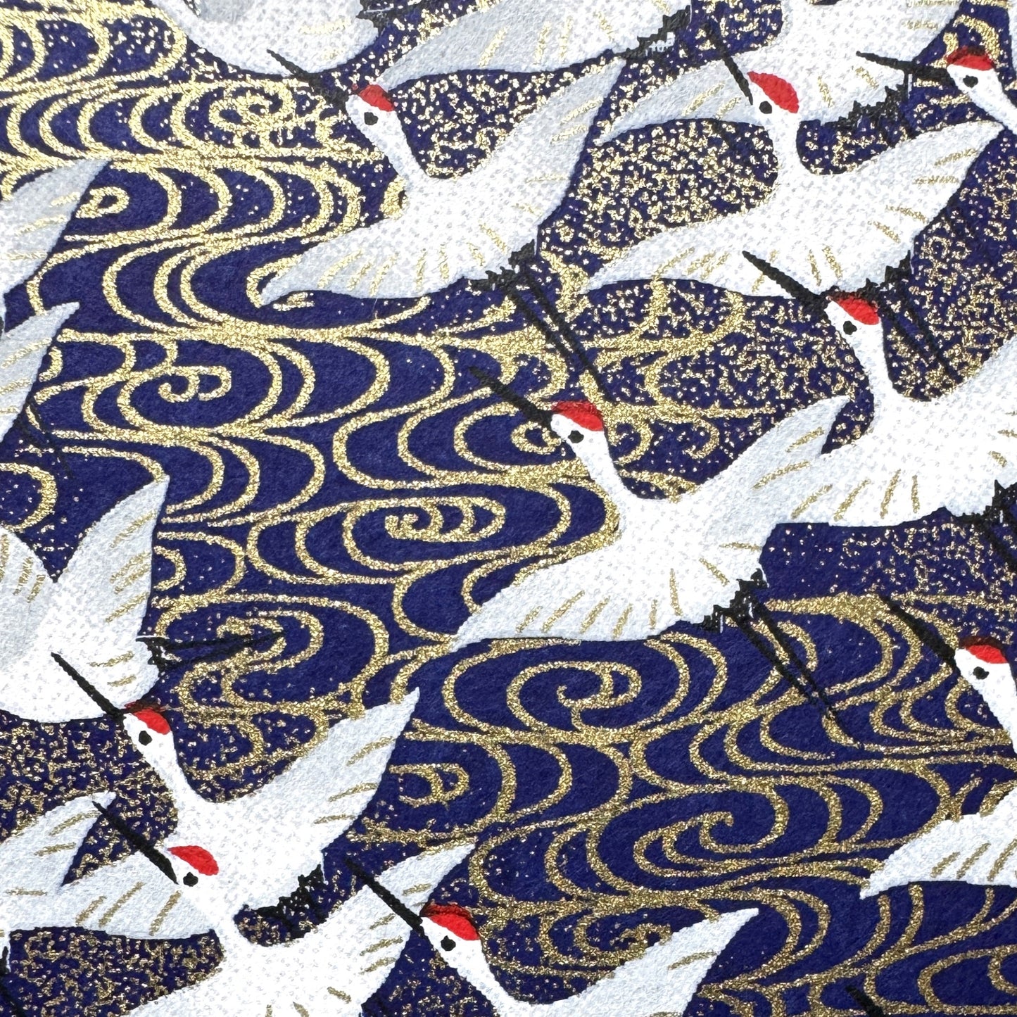 Japanese chiyogami paper with a silkscreened pattern of white cranes in flight on a midnight blue and gold background. Close-up
