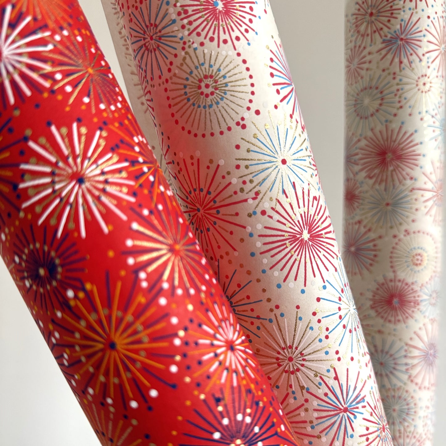japanese chiyogami silkscreen printed paper with a pattern of fireworks in reds, pinks and lilacs on an ivory background. Pictured alongside the same design in red