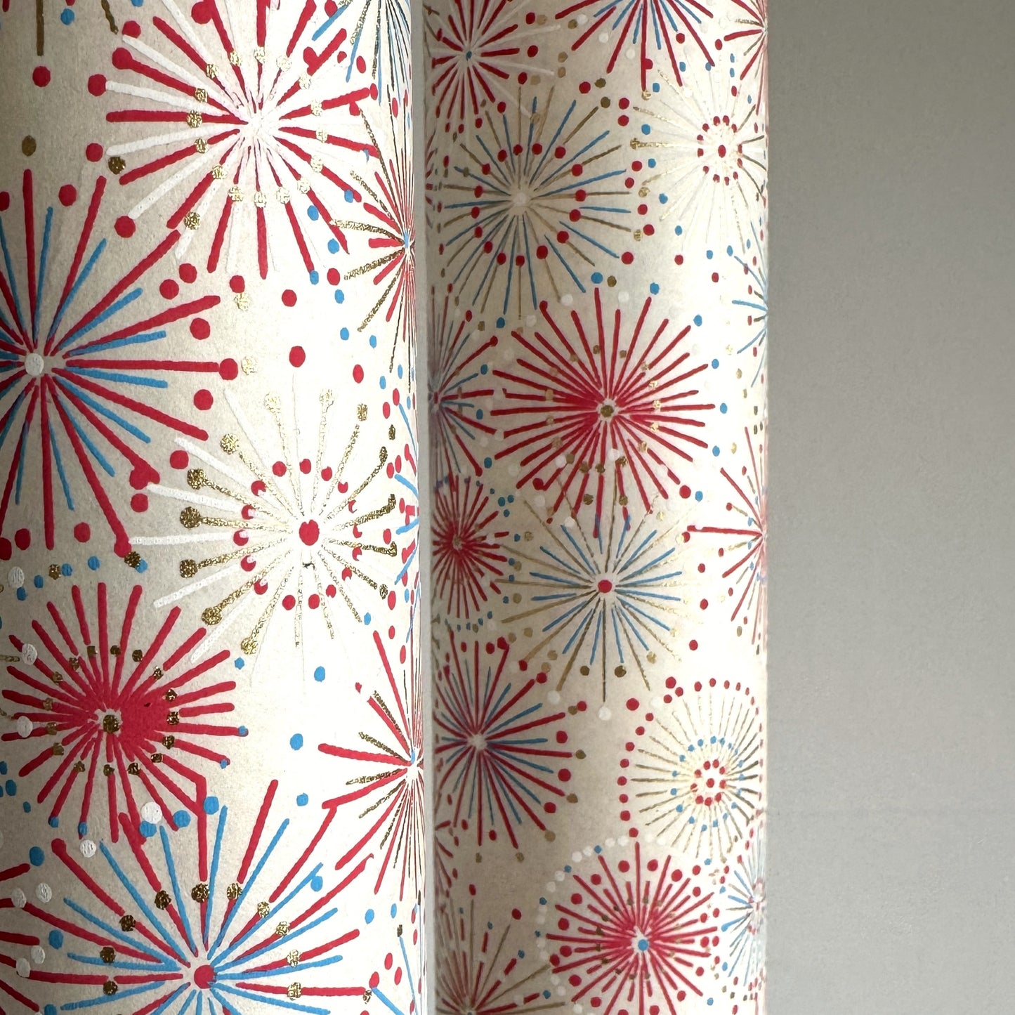 japanese chiyogami silkscreen printed paper with a pattern of fireworks in reds, pinks and lilacs on an ivory background. close-up