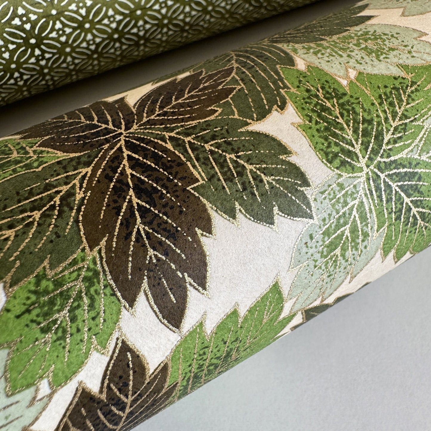 Japanese chiyogami paper with a pattern of green leaves in various tones with gold accent. Close up