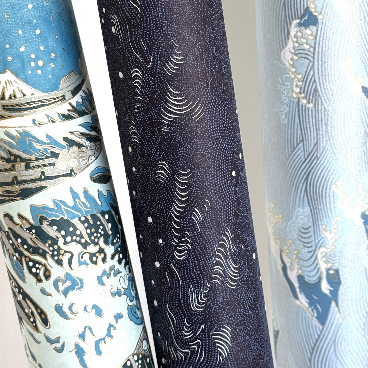 Japanese chiyogami paper. Inky blue with a subtle pattern of a riverbank of flowers. Pictured rolled with other papers.