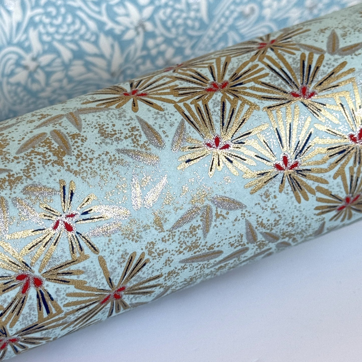 Japanese chiyogami paper silkscreen printed with gold pine needle design on a soft aqua backdrop. Rolled