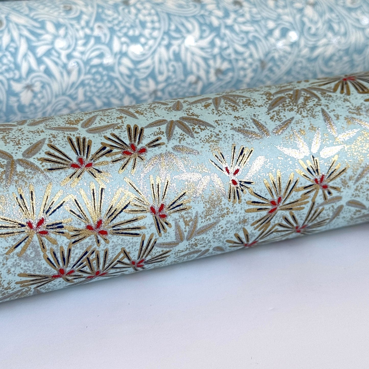Japanese chiyogami paper silkscreen printed with gold pine needle design on a soft aqua backdrop. Rolled