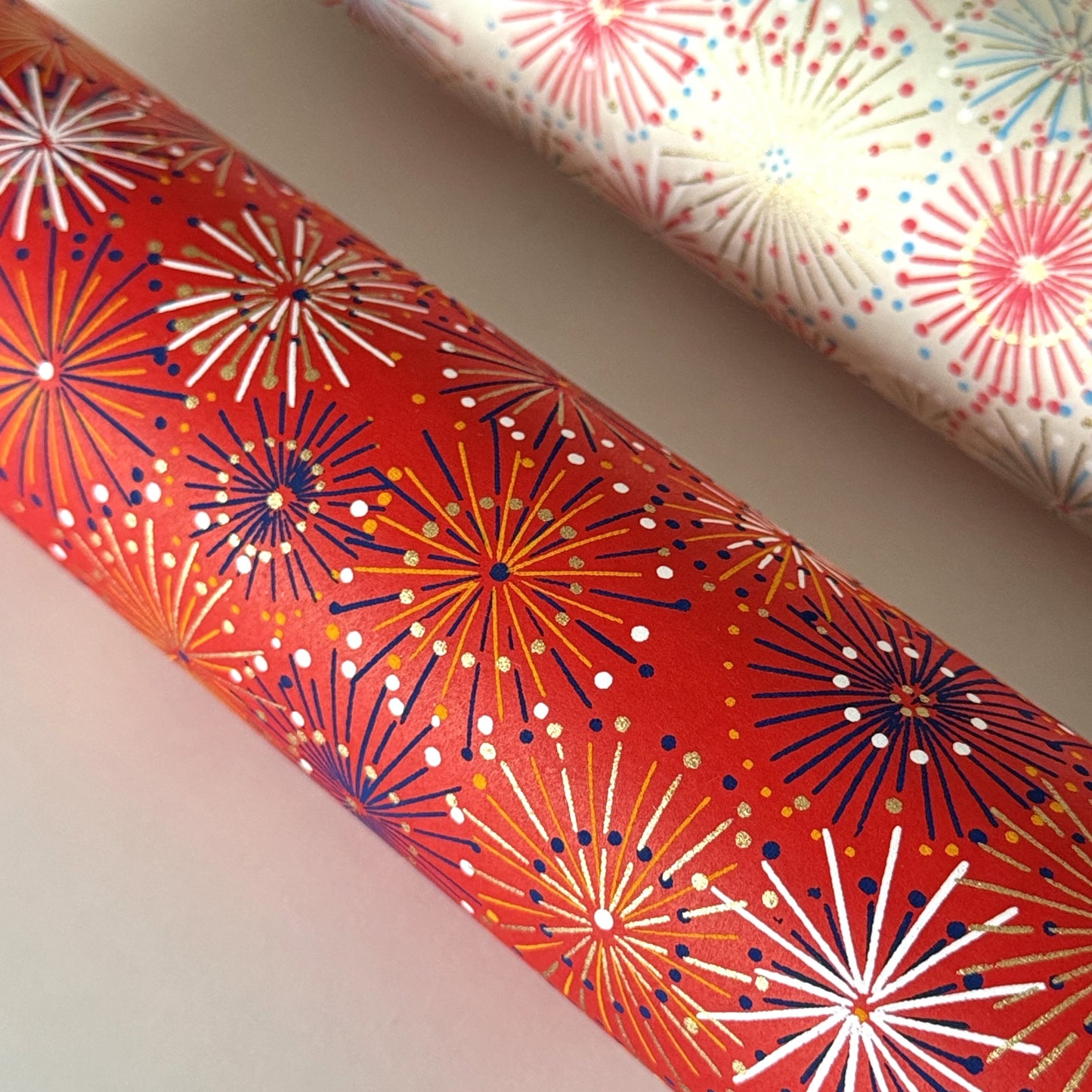japanese chiyogami silkscreen printed paper with a pattern of fireworks in golds and purples on a red background. Rolled