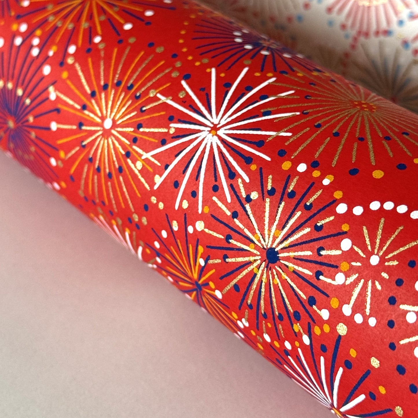 japanese chiyogami silkscreen printed paper with a pattern of fireworks in golds and purples on a red background. Close up