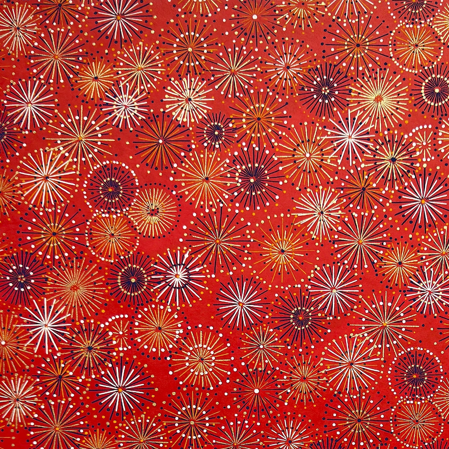 japanese chiyogami silkscreen printed paper with a pattern of fireworks in golds and purples on a red background.