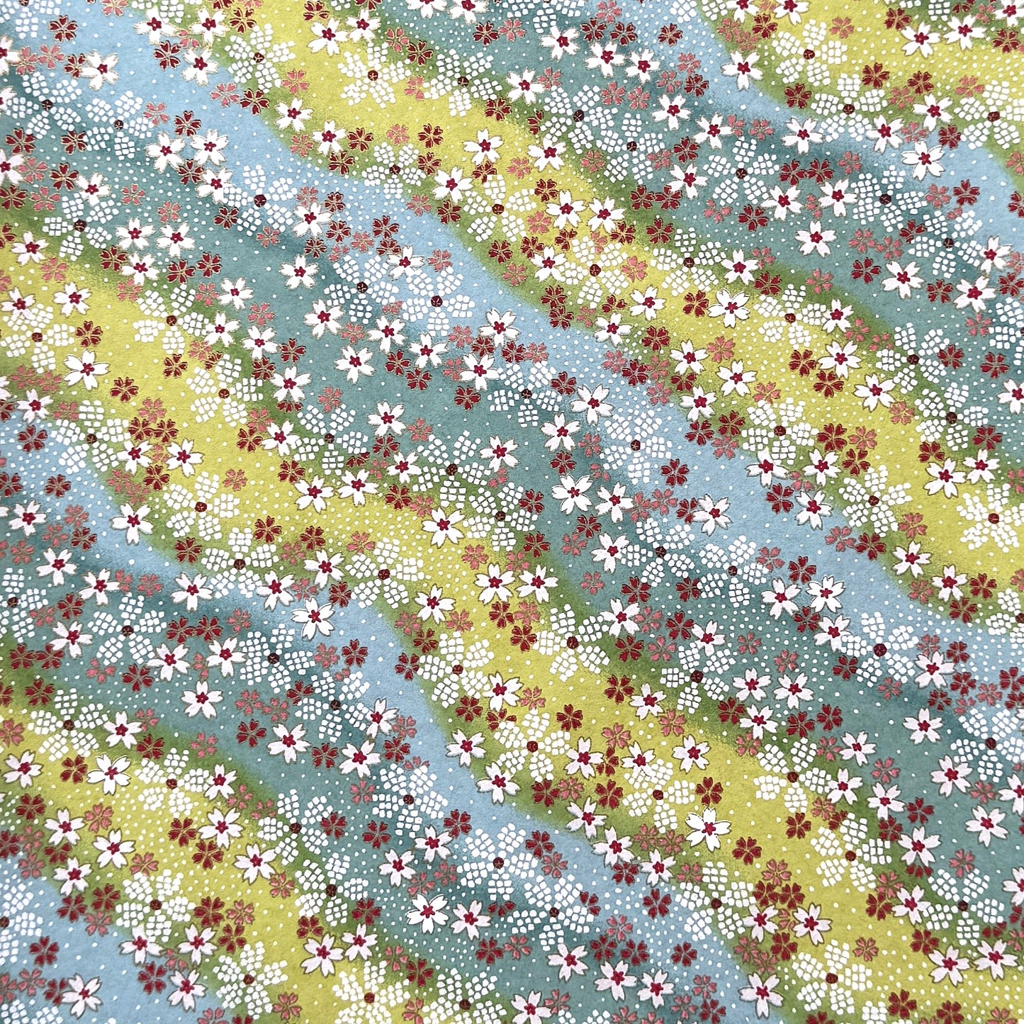 Japanese chiyogami paper silkscreened with a dainty pattern of white sakura flowers on an backdrop of aqua and lime diagonal wavy stripes