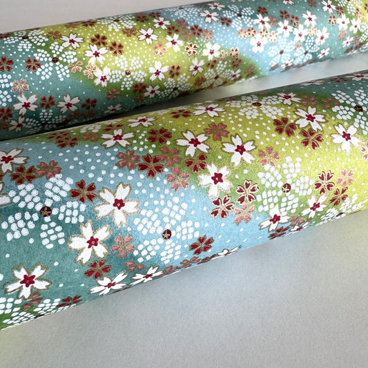 Japanese chiyogami paper silkscreened with a dainty pattern of white sakura flowers on an backdrop of aqua and lime diagonal wavy stripes. Close-up