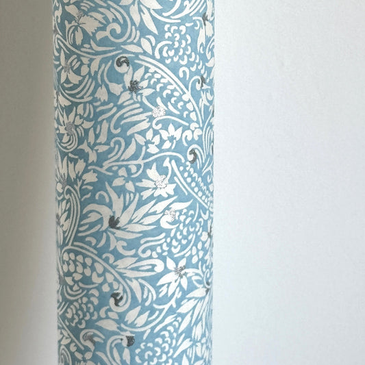 Japanese chiyogami paper - silkscreen printed - light blue backdrop with a small botanical pattern in white with silver accents. Pictured rolled
