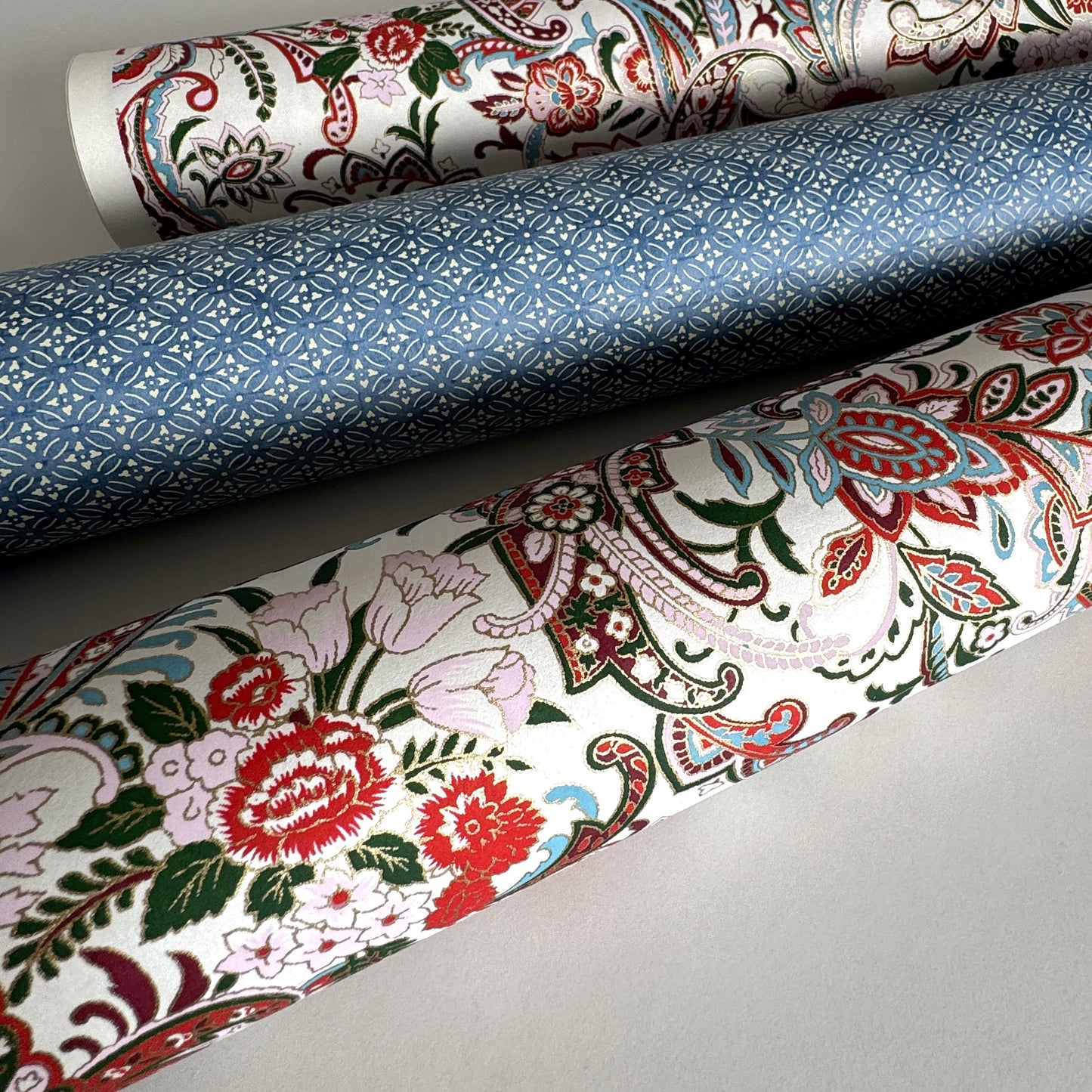 Japanese chiyogami paper silkscreened with a paisley floral style pattern in red, aqua, green and gold on a white background. Rolled