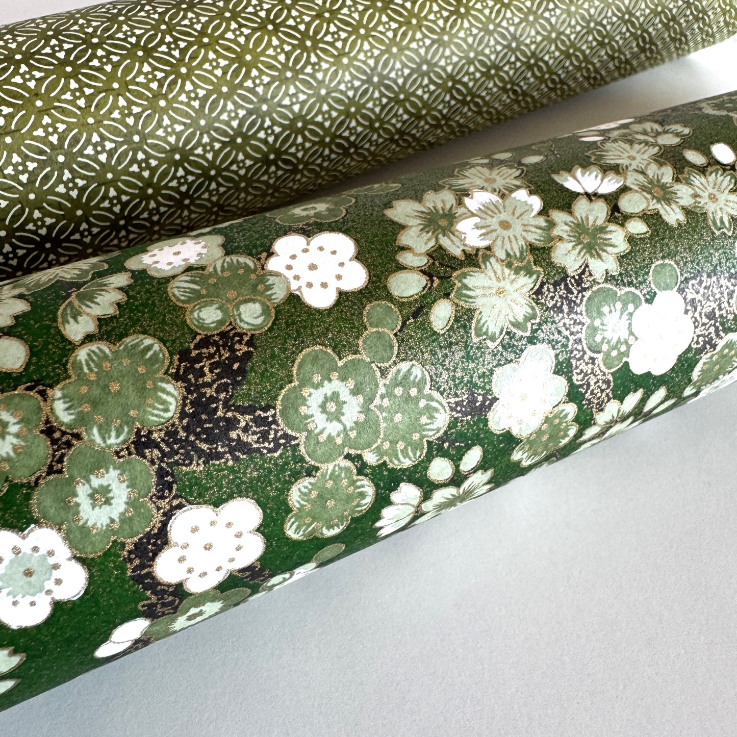 Japanese chiyogami paper with white and pale green blossom flowers on dark green backdrop.