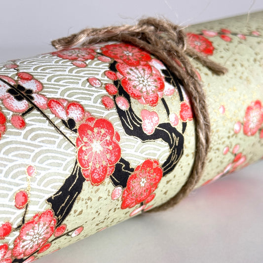 Japanese chiyogami silkscreen paper with diagonal branches of pink plum blossom on a sage green backdrop. Close up