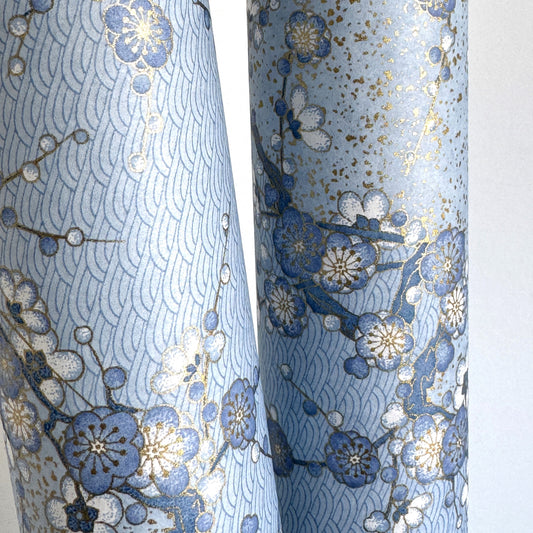 Japanese chiyogami paper with diagonal branches of sky blue plum blossom on a light blue background. close up shows gold accent