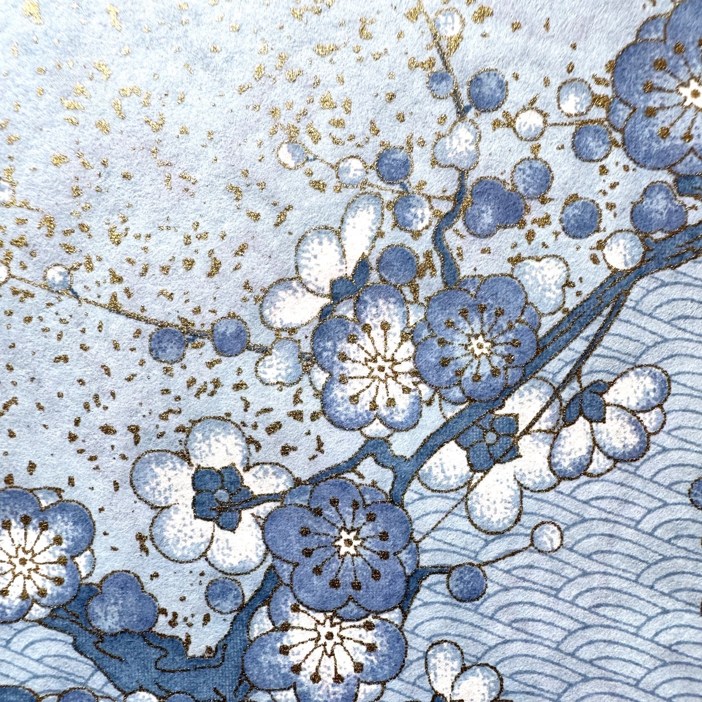 Japanese chiyogami paper with diagonal branches of sky blue plum blossom on a light blue background. Close up of the plum blossom