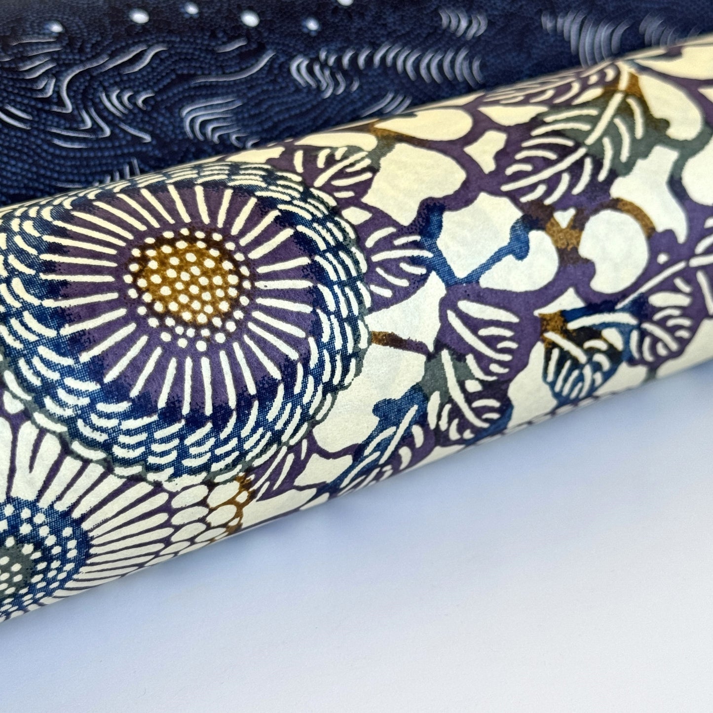 Japanese chiyogami silkscreen printed paper with a floral kiko pattern in purple and blue on a cream backdrop. Rolled