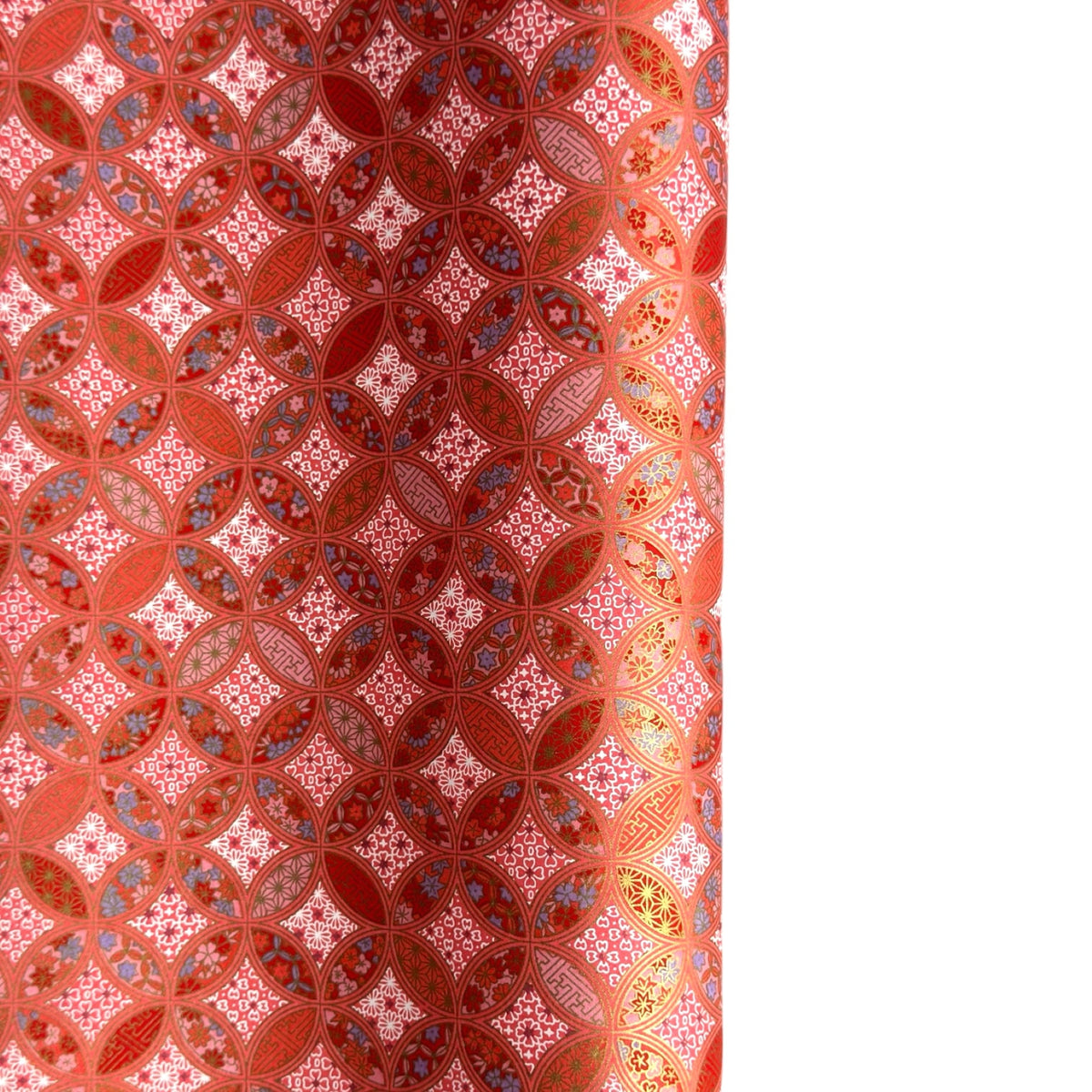 A close-up of a sheet of Japanese chiyogami paper featuring a repeating geometric medallion design in shades of terracotta red, coral pink, and metallic gold
