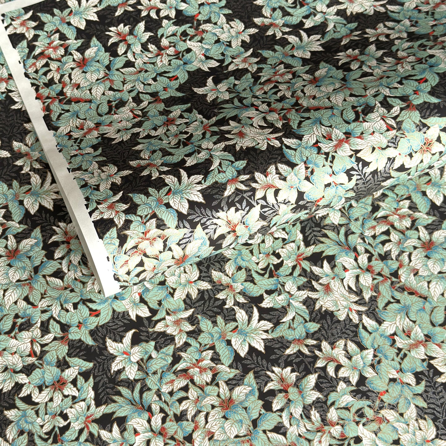 a sheet of Japanese chiyogami screen printed paper with a pattern of light green foliage on a black ground with silver botanical details