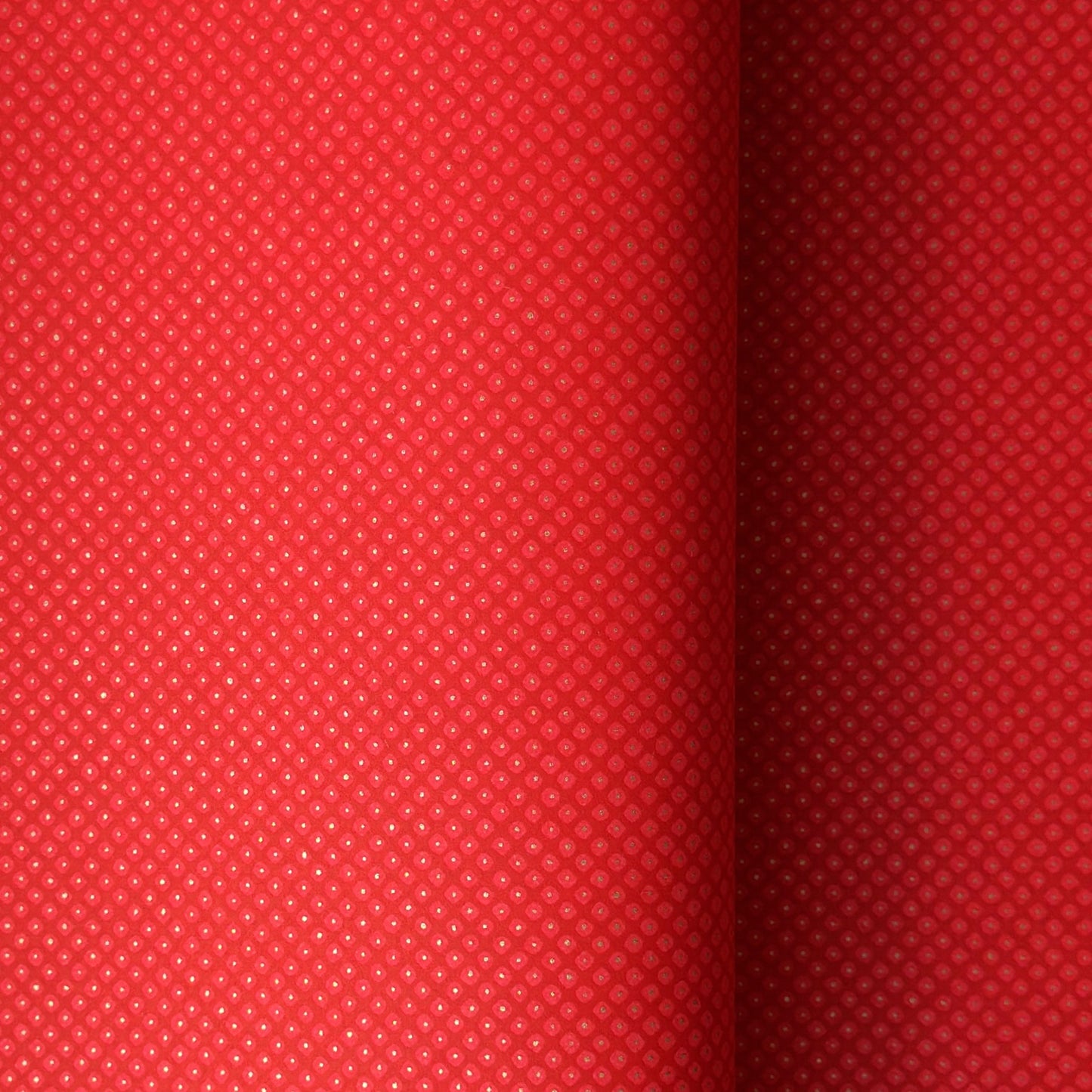 A close-up of a bright red sheet of chiyogami paper with a fine dotted pattern in gold.