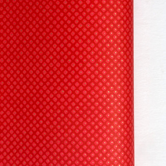 A close-up of a bright red sheet of chiyogami paper with a fine dotted pattern in gold.