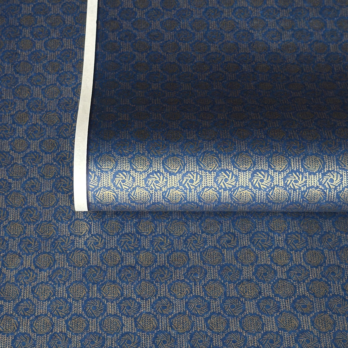 A sheet of Japanese chiyogami paper with a small repeat pattern of gold circular crests on a dark blue background.