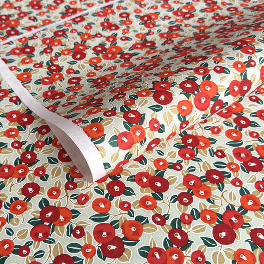 Japanese silkscreen chiyogami paper with a repeat pattern of camellia flowers in red and orange on a soft green ground