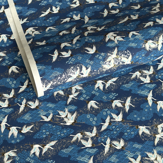 a sheet of Japanese chiyogami yuzen paper with a traditional pattern of white cranes flying with a deep blue background of patterned clouds