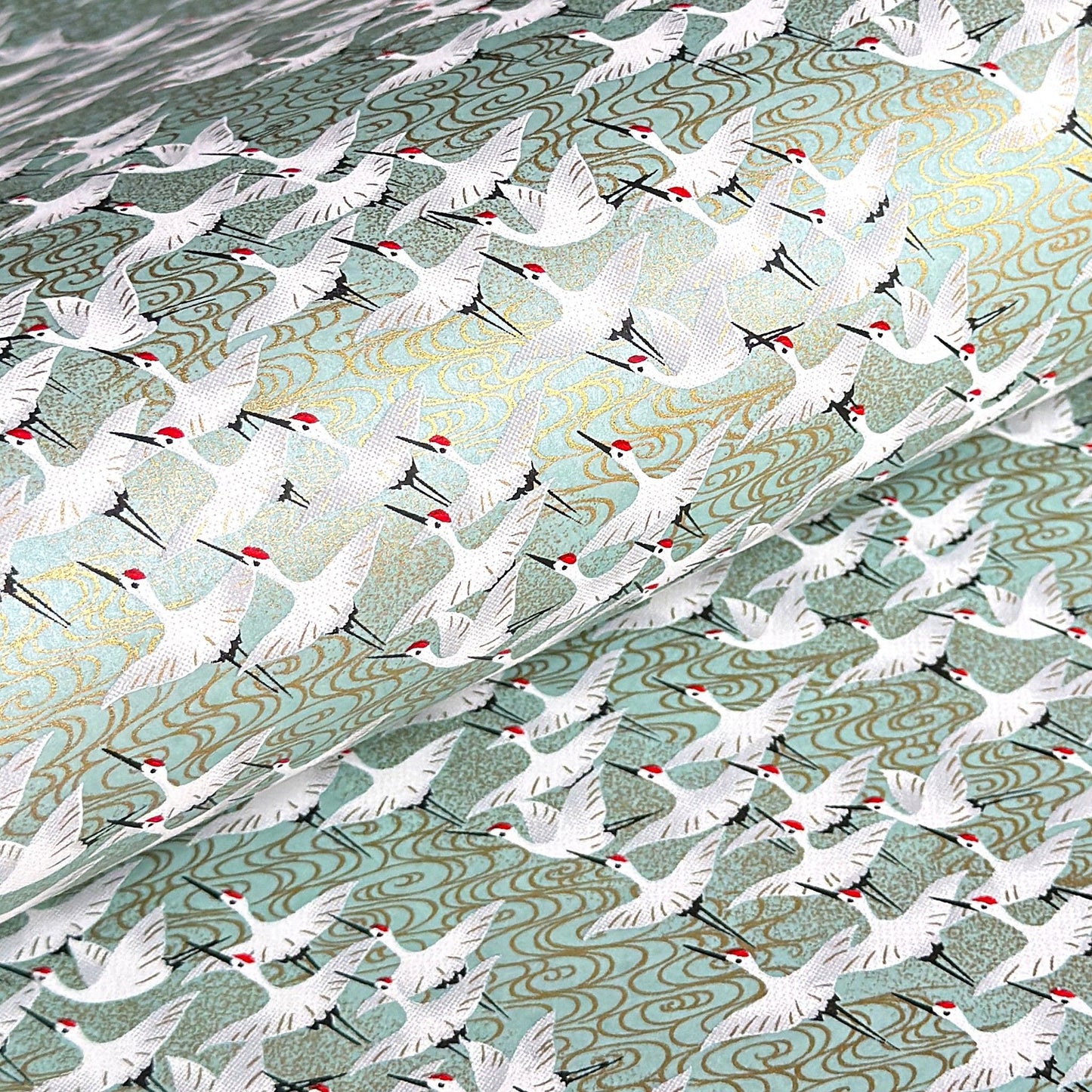 japanese silk-screen handmade paper showing white cranes in flight on a light teal and gold backdrop