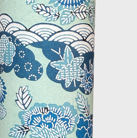 A colourful traditional pattern depicting stylised waves (seigaiha), flowers and foliage in a soft aqua and blue palette. A sheet of katazome paper. Close up