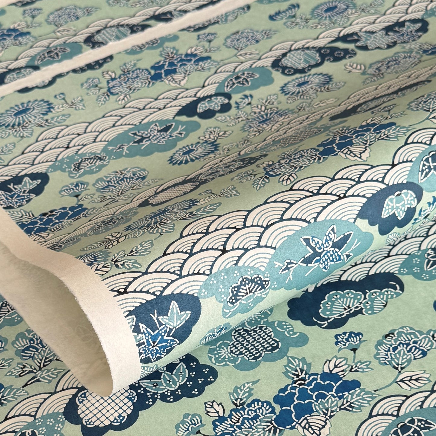 A colourful traditional pattern depicting stylised waves (seigaiha), flowers and foliage in a soft aqua and blue palette. A sheet of katazome paper