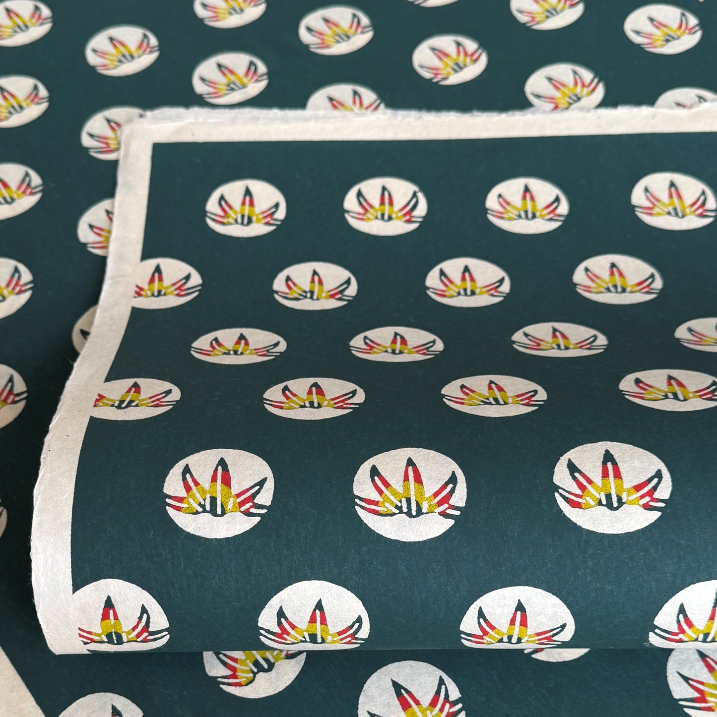 Traditional pattern a Japanese circular crest of a colourful lotus flower on a dark teal. A sheet of katazome paper