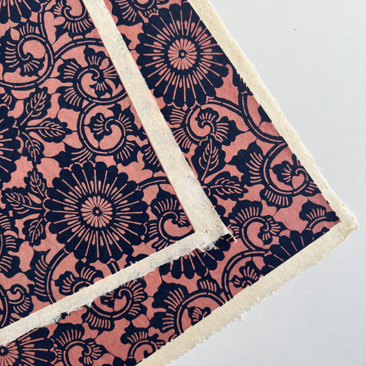 Japanese katazome-shi paper with a silkscreen of a chrysanthemum (kiko) flowers pattern in navy on blush pink. Close up