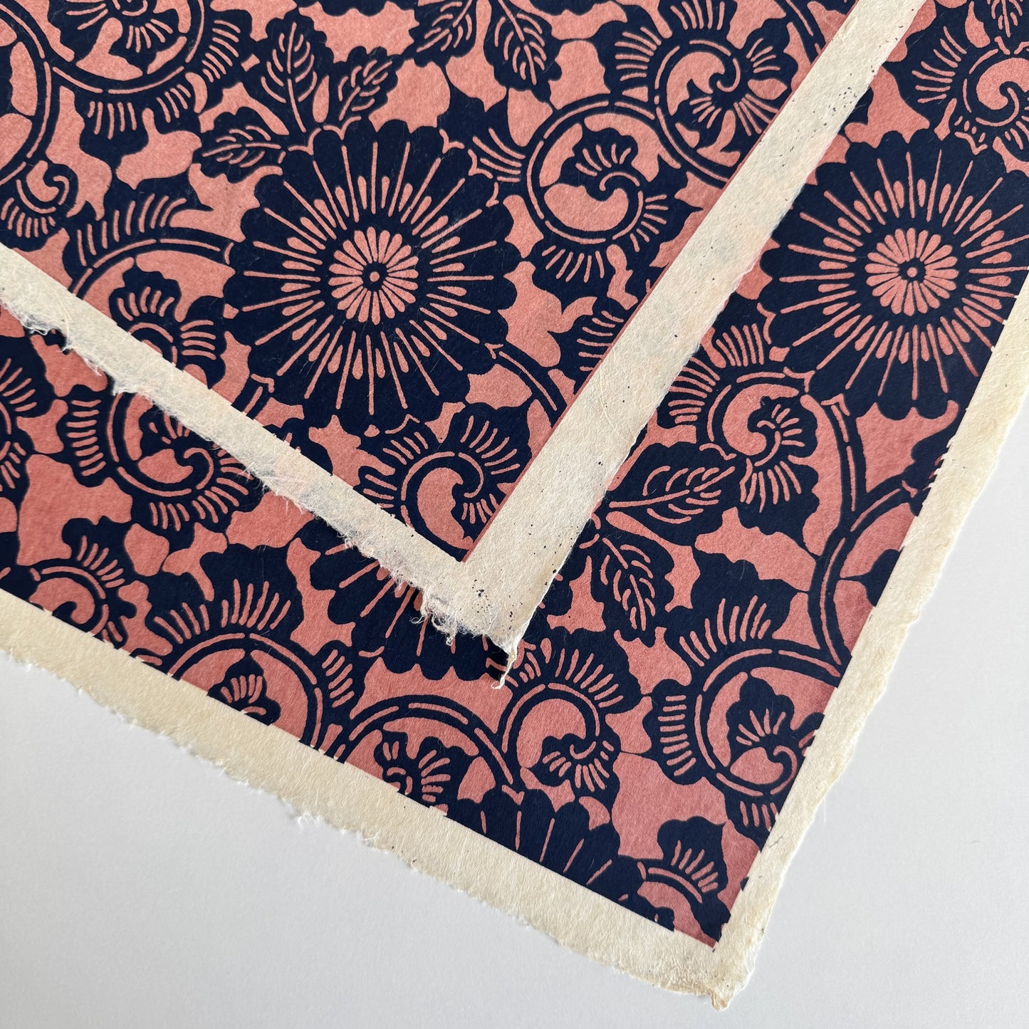Japanese katazome-shi paper with a silkscreen of a chrysanthemum (kiko) flowers pattern in navy on blush pink. Close up