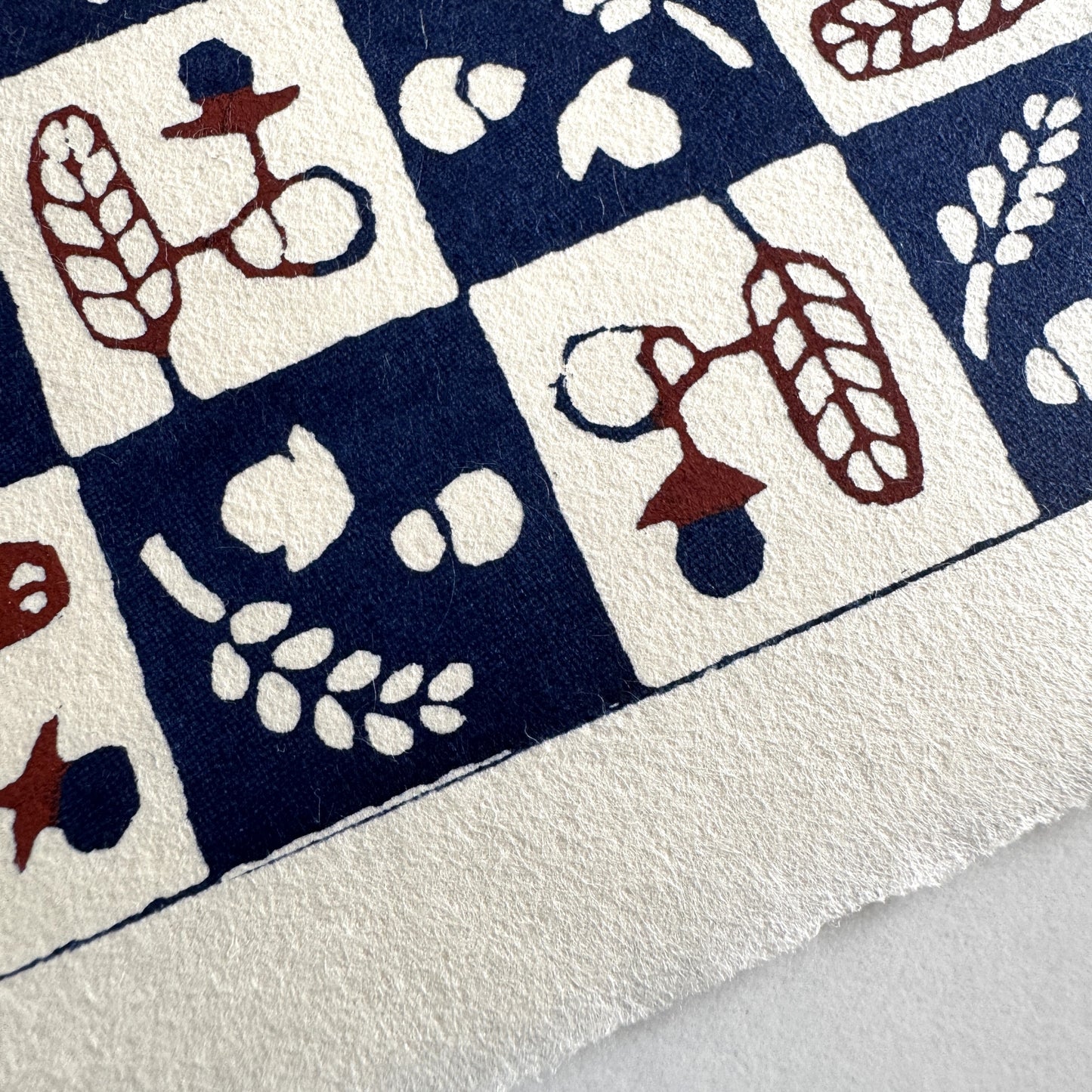 Japanese katazome-shi paper in navy blue and cream chequerboard pattern with motifs of autumn - acorns and wheat. Close up