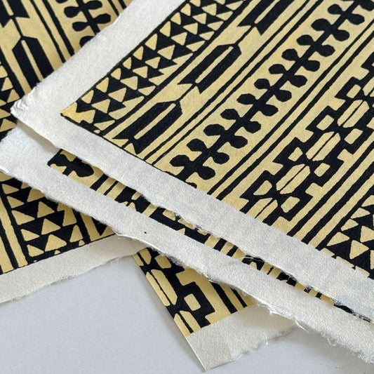 Japanese katazome-shi stencil-dyed paper with striped motifs in black on yellow paper. Close-up showing the white deckled edges
