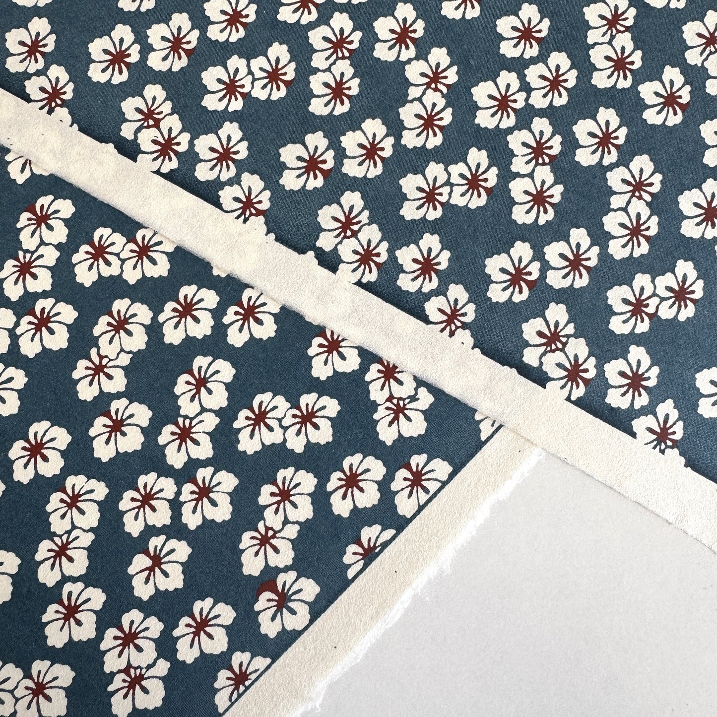 Japanese katazome-shi paper stencil-dyed with a small flower pattern in inky blue, white and red. Close-up
