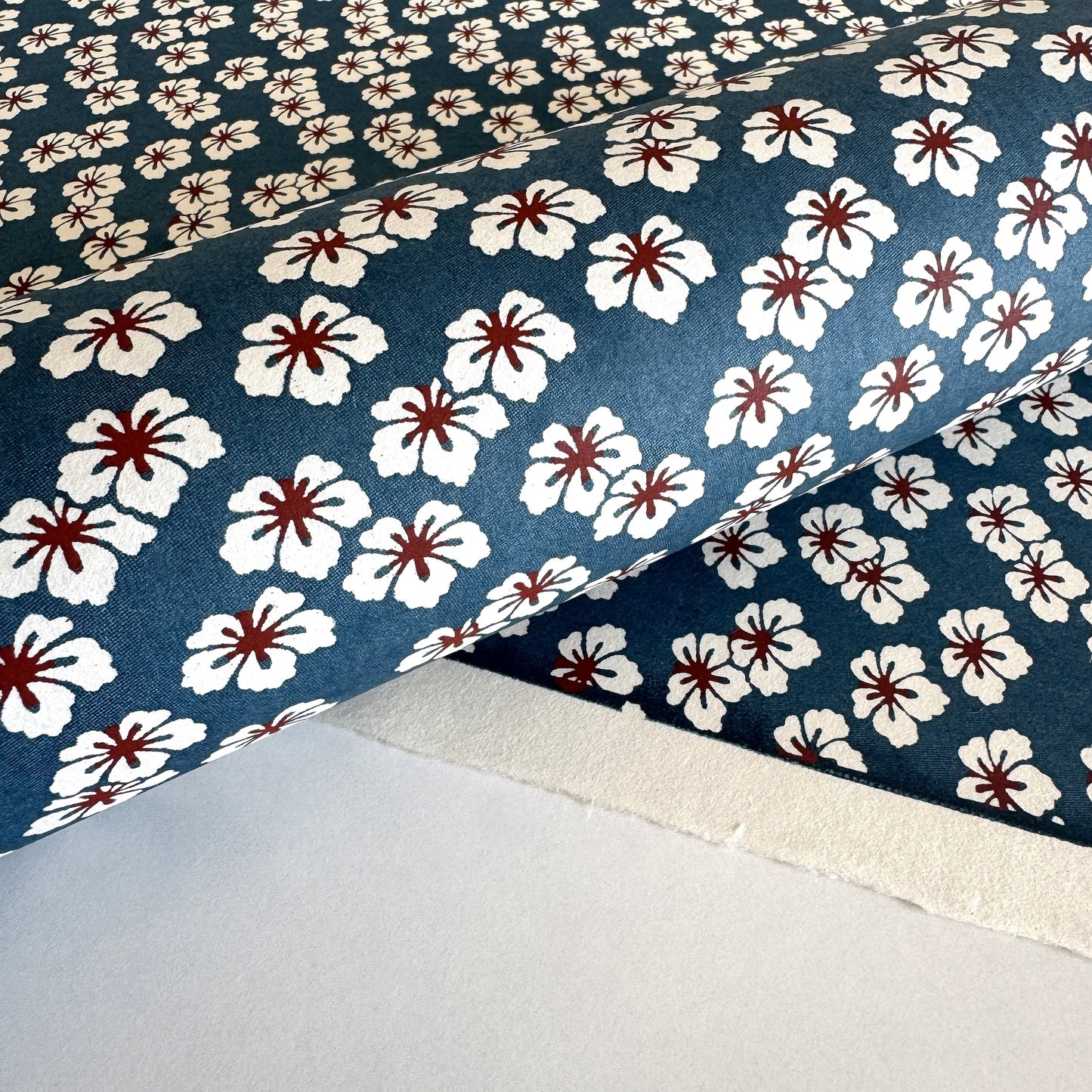 Japanese katazome-shi paper stencil-dyed with a small flower pattern in inky blue, white and red.  Close-up rolled