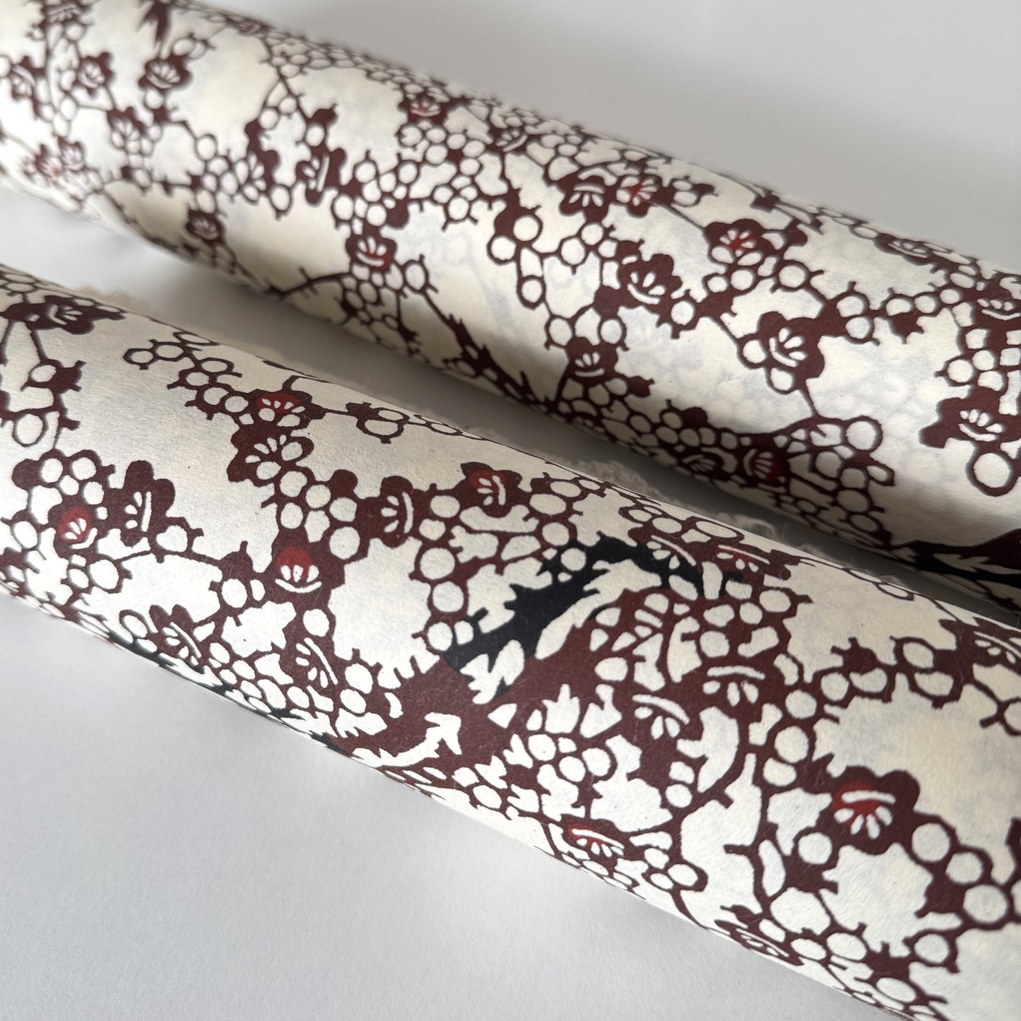 Japanese kazazome-shi stenciled dyed paper with a pattern of branches of plum blossom in deep maroon and black on an ivory paper. Rolled