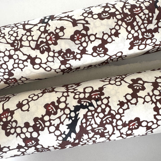 Japanese kazazome-shi stenciled dyed paper with a pattern of branches of plum blossom in deep maroon and black on an ivory paper. close-up