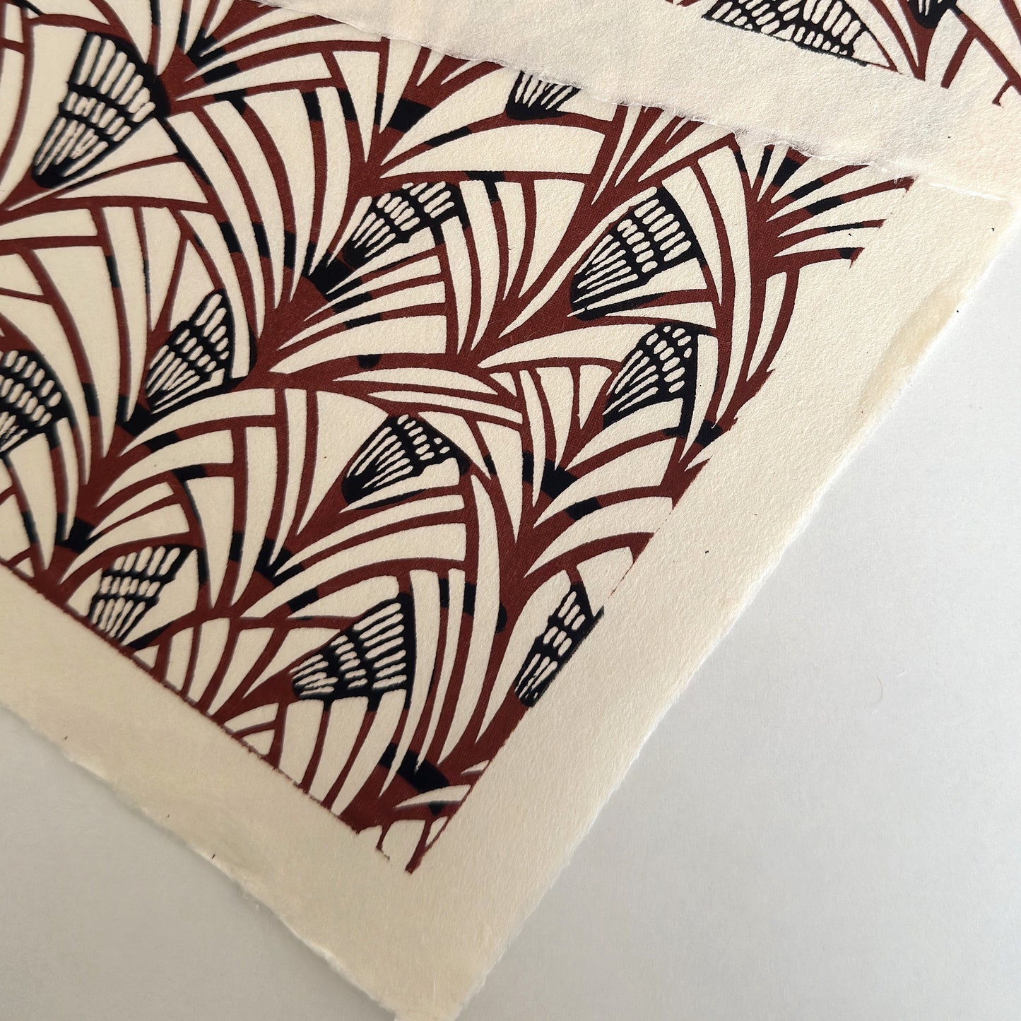 Japanese katazome-shi stencil-dyed paper with a fan-like pattern in deep maroon and black on cream paper. showing the deckled edges
