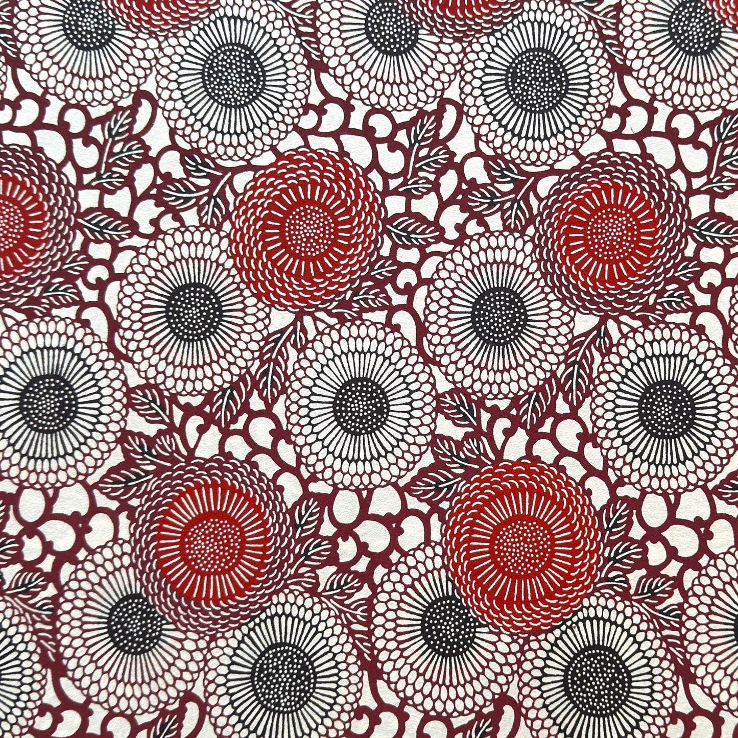 Japanese katazome-shi paper stencil-dyed with a pattern of stylised kiko flowers in red, maroon and black on an ivory paper.